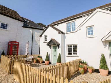 A white cottage with potted plants a wooden fence and a red telephone box at Swallow Cottage in Ilfracombe