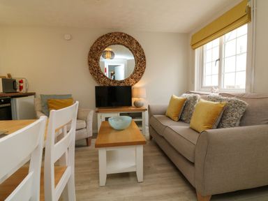 A living room with a sofa and armchair a coffee table a TV and a round mirror at Swallow Cottage in Ilfracombe