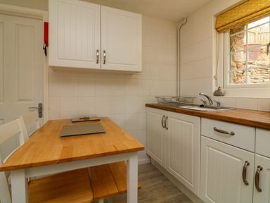 A kitchen with wooden countertops white cabinets a table and chairs near a window at Swallow Cottage in Ilfracombe