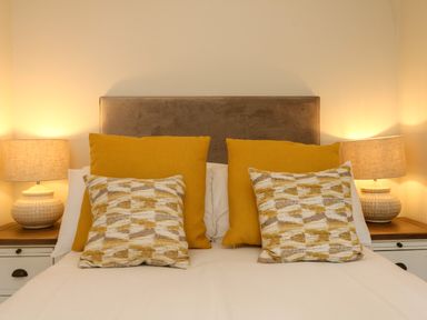A bed with patterned and solid yellow pillows and two lamps on bedside tables at Swallow Cottage in Ilfracombe