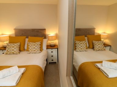 A bedroom with a double bed orange pillows and bedside tables with lamps at Swallow Cottage in Ilfracombe