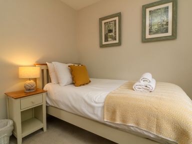 A bedroom with a single bed white and yellow pillows and a bedside table with a lamp at Swallow Cottage in Ilfracombe