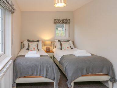 A bedroom with two single beds, a bedside table with a lamp, and a window with a view at Kingfisher Cottage in Ilfracombe