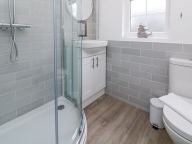 A bathroom with a corner shower enclosure a sink with cabinet a toilet and a frosted window at Kingfisher Cottage in Ilfracombe