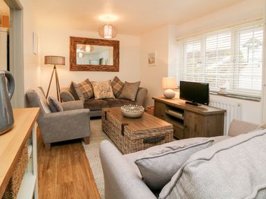 A living room with sofas a wooden coffee table a floor lamp and a TV on a cabinet at Kingfisher Cottage in Ilfracombe