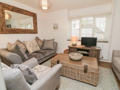 A living room with sofas a television on a wooden cabinet and a wicker coffee table at Kingfisher Cottage in Ilfracombe