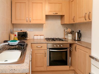 A kitchen with wooden cabinets a sink dish rack oven stove microwave and kettle at Kingfisher Cottage in Ilfracombe