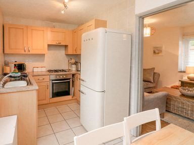 A kitchen with wooden cabinets a white SMEG refrigerator a gas stove and an oven next to a dining table and chairs at Kingfisher Cottage in Ilfracombe