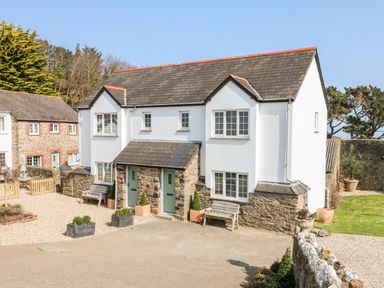 The exterior of a white and stone two story house with two green front doors and benches outside at Kingfisher Cottage in Ilfracombe