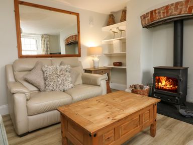A living room with a beige leather sofa and wooden coffee table next to a wood-burning stove at Partridge Cottage in Ilfracombe
