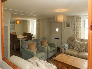 A living room with chairs a sofa a wooden coffee table and a dining area with wicker chairs at Partridge Cottage in Ilfracombe