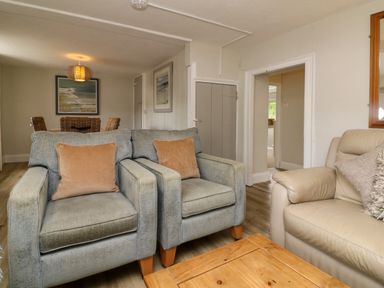 A living room with two gray armchairs with brown cushions a beige sofa wooden table and a dining area at Partridge Cottage in Ilfracombe