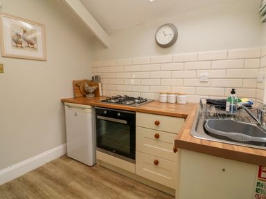 A kitchen with a small fridge oven stove sink and three canisters at Partridge Cottage in Ilfracombe