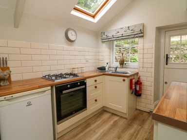 A kitchen with wooden countertops a gas stove an oven a small refrigerator and a window with a bird patterned blind at Partridge Cottage in Ilfracombe