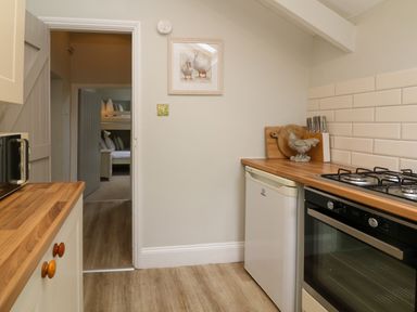 A kitchen with wooden countertops a microwave gas stove and a small fridge next to a doorway leading to a room with bunk beds at Partridge Cottage in Ilfracombe
