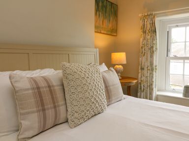 A bedroom with pillows on a bed and a lamp on a wooden side table near a window at Partridge Cottage in Ilfracombe