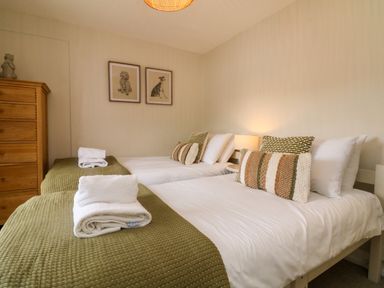 A bedroom with two single beds with green bedspreads and pillows a wooden dresser and two framed pictures on the wall at Partridge Cottage in Ilfracombe