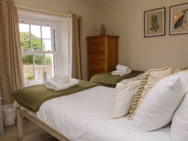 A bedroom with two single beds towels on beds a wooden chest of drawers and framed dog pictures on wall at Partridge Cottage in Ilfracombe
