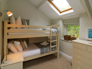 A bedroom with bunk beds a dresser a window with baskets and a skylight at Partridge Cottage in Ilfracombe