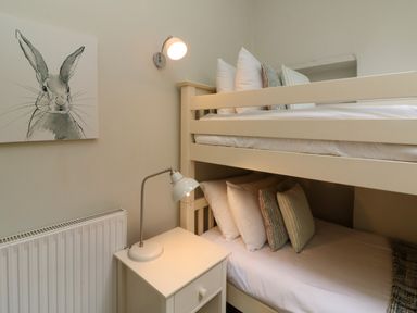 A bedroom with bunk beds pillows a bedside table and lamps and a rabbit painting on the wall at Partridge Cottage in Ilfracombe