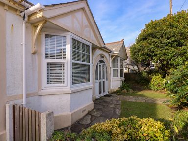 A front view of a house with white framed windows a glass front door a stone path and garden bushes at Pound Rocks in Tintagel