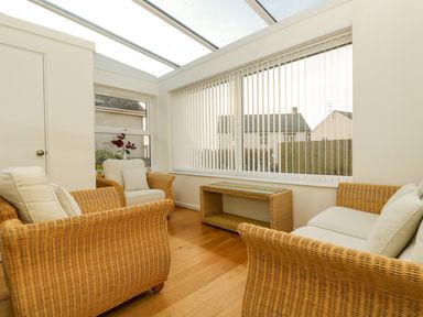 A sunroom with wicker furniture including chairs and a sofa and vertical blinds at Pound Rocks in Tintagel