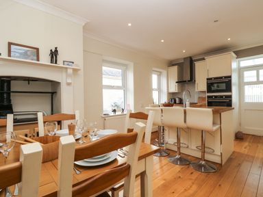 A dining table set with plates and glasses next to a kitchen island with stools in a kitchen at Pound Rocks in Tintagel