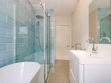 A bathroom with a bathtub shower area with blue tiles and a white sink with a faucet at Pound Rocks in Tintagel