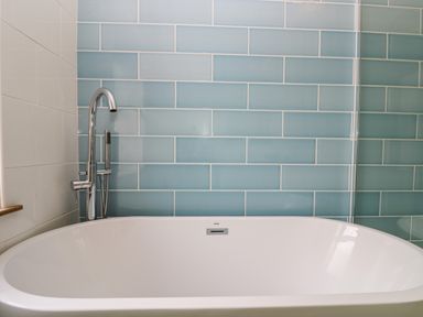 A bathtub with a chrome faucet and a handheld showerhead against a blue tiled wall at Pound Rocks in Tintagel