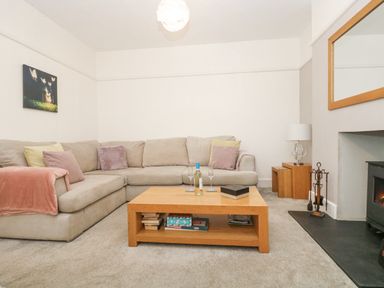 A living room with a beige sectional sofa a wooden coffee table with books and wine glasses a fireplace and a lamp on wooden nesting tables at Pound Rocks in Tintagel