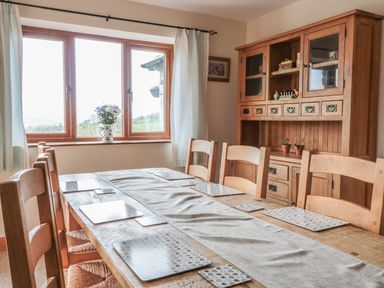 A dining room with a wooden table set with placemats and chairs by a window with curtains and a wooden cabinet with shelves and drawers at Blaen Henllan in Builth Wells