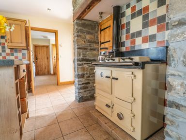 A kitchen with a beige stove, stone walls, tiled floor, and wooden doors at Blaen Henllan in Builth Wells