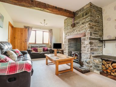 A living room with two sofas a wooden coffee table and a stone fireplace with firewood at Blaen Henllan in Builth Wells