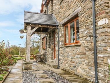 Stone exterior wall of a house with wooden framed windows a covered porch with wooden posts and outdoor seating at Blaen Henllan in Builth Wells