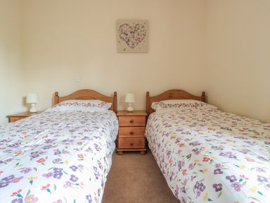 A bedroom with two single beds with floral bedding a wooden nightstand and lamps at Blaen Henllan in Builth Wells