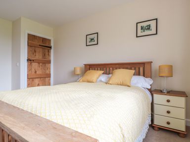 A bedroom with a wooden bed a yellow blanket and pillows a wooden door and a bedside table with a lamp at Blaen Henllan in Builth Wells