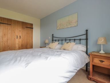 A bedroom with a metal bed frame white bedding sheep cushions wooden bedside tables with lamps and wooden wardrobes at Blaen Henllan in Builth Wells