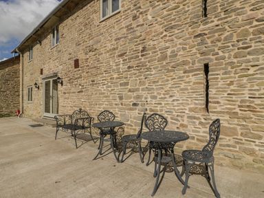 A stone wall with metal tables and chairs outside a building at Timber Barn in Eardisland