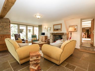 A living room with two yellow sofas a wooden coffee table a fireplace and glass doors at Timber Barn in Eardisland