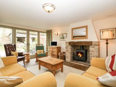 A living room with yellow sofas a stone fireplace a wooden coffee table and large glass doors at Timber Barn in Eardisland