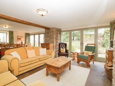 A living room with yellow sofas a wooden coffee table armchairs and large windows at Timber Barn in Eardisland