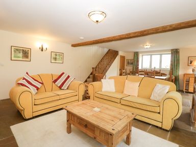 A living room with yellow sofas a wooden coffee table wooden staircase and dining table at Timber Barn in Eardisland