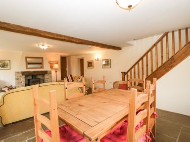 A dining area with a wooden table and six chairs with red cushions next to a living room with a yellow sofa and a fireplace under a wooden beam at Timber Barn in Eardisland