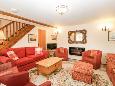 A living room with red sofas armchairs a wooden coffee table and a staircase at Timber Barn in Eardisland