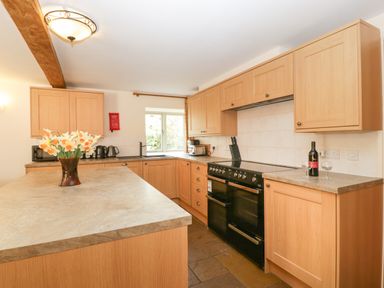 A kitchen with wooden cabinets a black stove a vase with flowers on the counter and a bottle of wine with glasses at Timber Barn in Eardisland