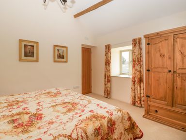 A bedroom with a floral bedspread wooden wardrobe and framed pictures on the wall at Timber Barn in Eardisland