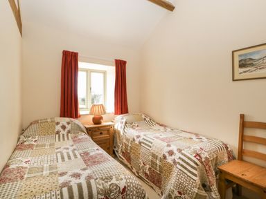 A bedroom with two single beds a wooden nightstand with a lamp red curtains and a wooden chair at Timber Barn in Eardisland