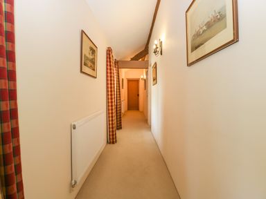 A narrow hallway with carpeted floor radiator wall lights and framed pictures at Timber Barn in Eardisland