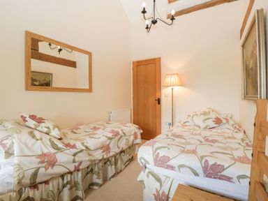 A bedroom with two single beds floral bedding a wooden door a floor lamp and a large wall mirror at Timber Barn in Eardisland