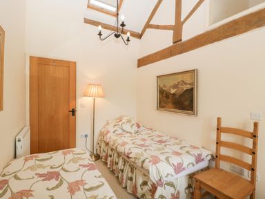 A bedroom with two single beds floral bedding a wooden chair and a floor lamp at Timber Barn in Eardisland